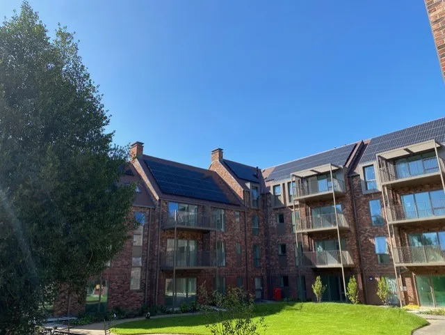 New brick apartment buildings with balconies and solar panels around a landscaped courtyard